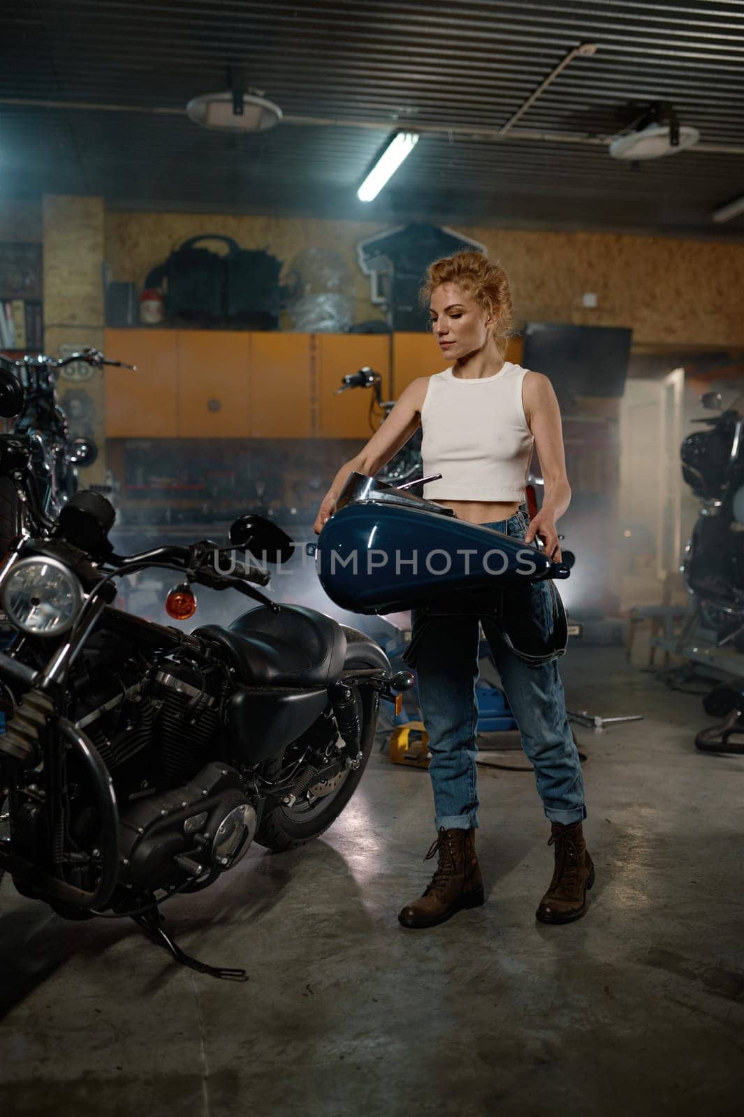 Attentive female master fixing fuel tank during repair work with bike at garage workshop
