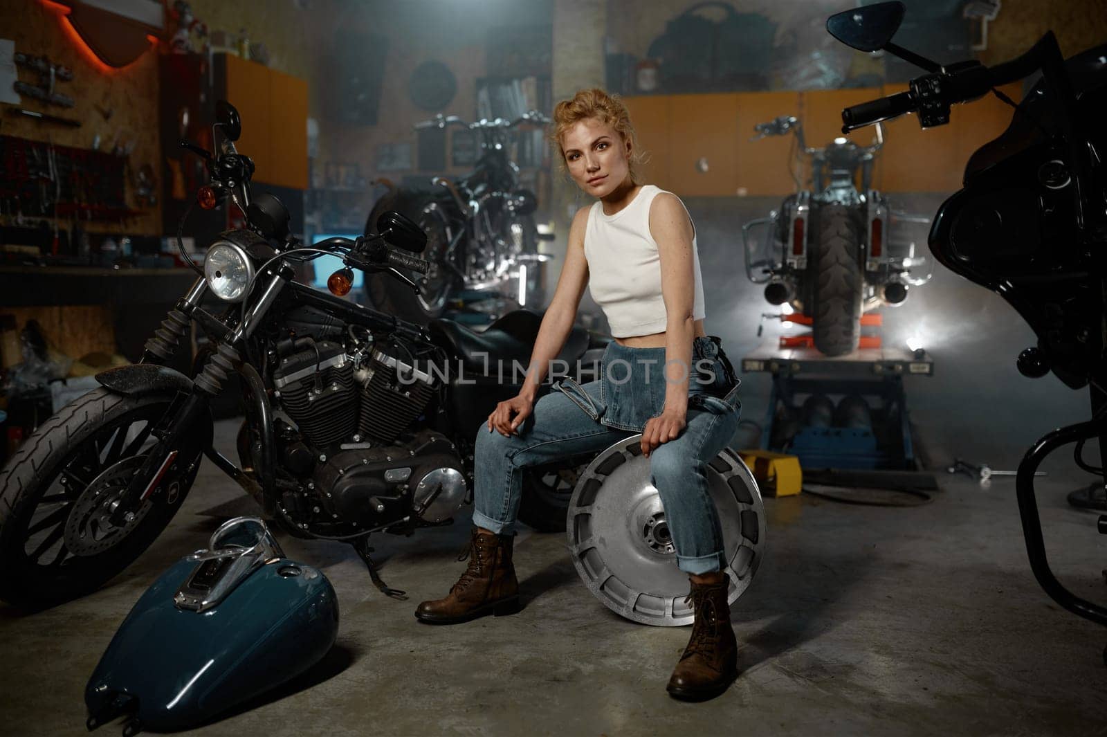 Young trendy blond woman mechanic at motorbike garage. Repair work and bike maintenance service