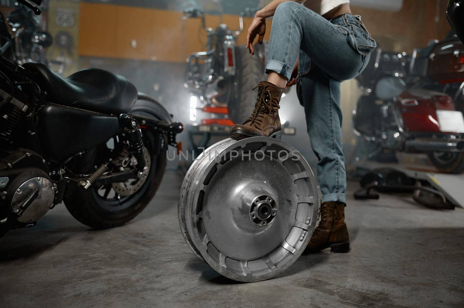 Cropped shot over motorbike garage workshop with female holding leg on chrome wheel disk