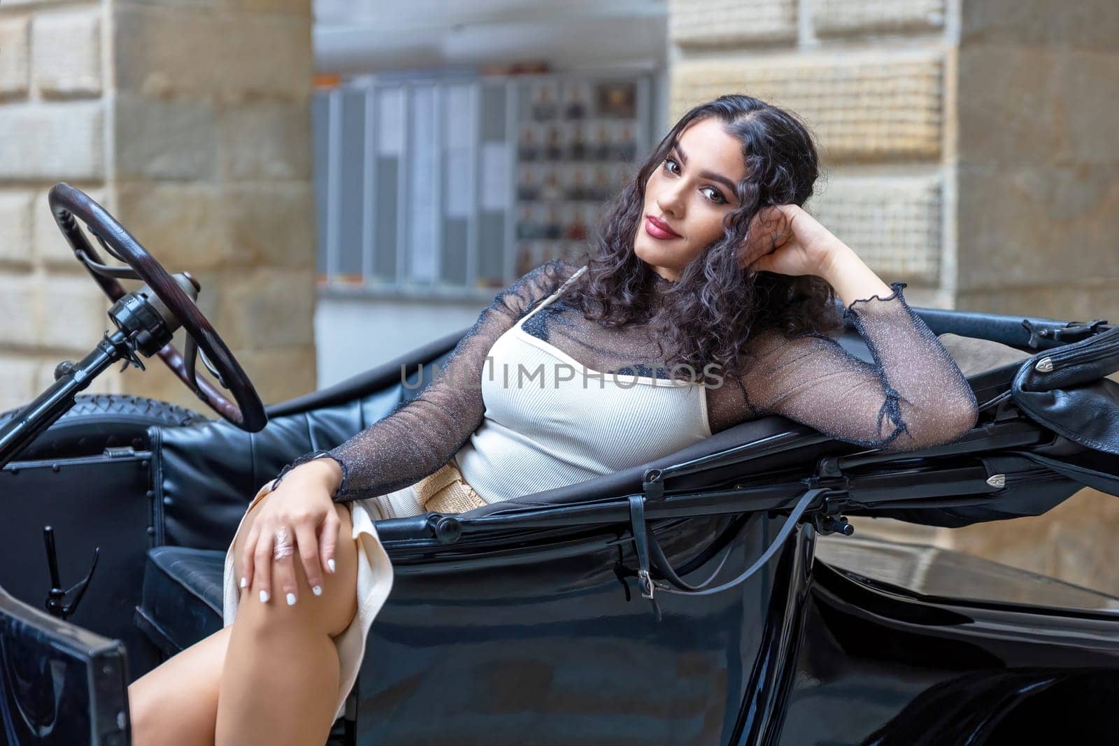 Attractive long black hair girl is resting on vintage car looking at the camera.  Horizontally.