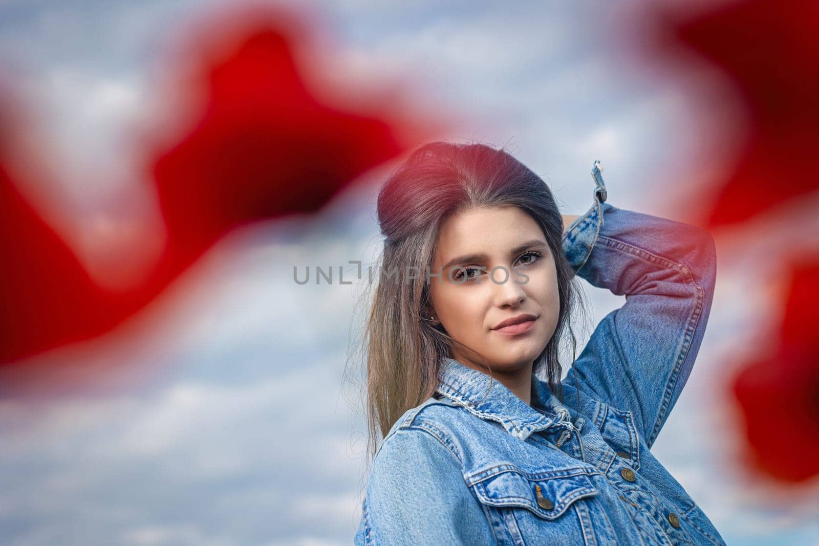 Closeup portrait of  attractive long haired girl from behind blurred red poppy leaves. The blue sky is in the background.. Horizontally.