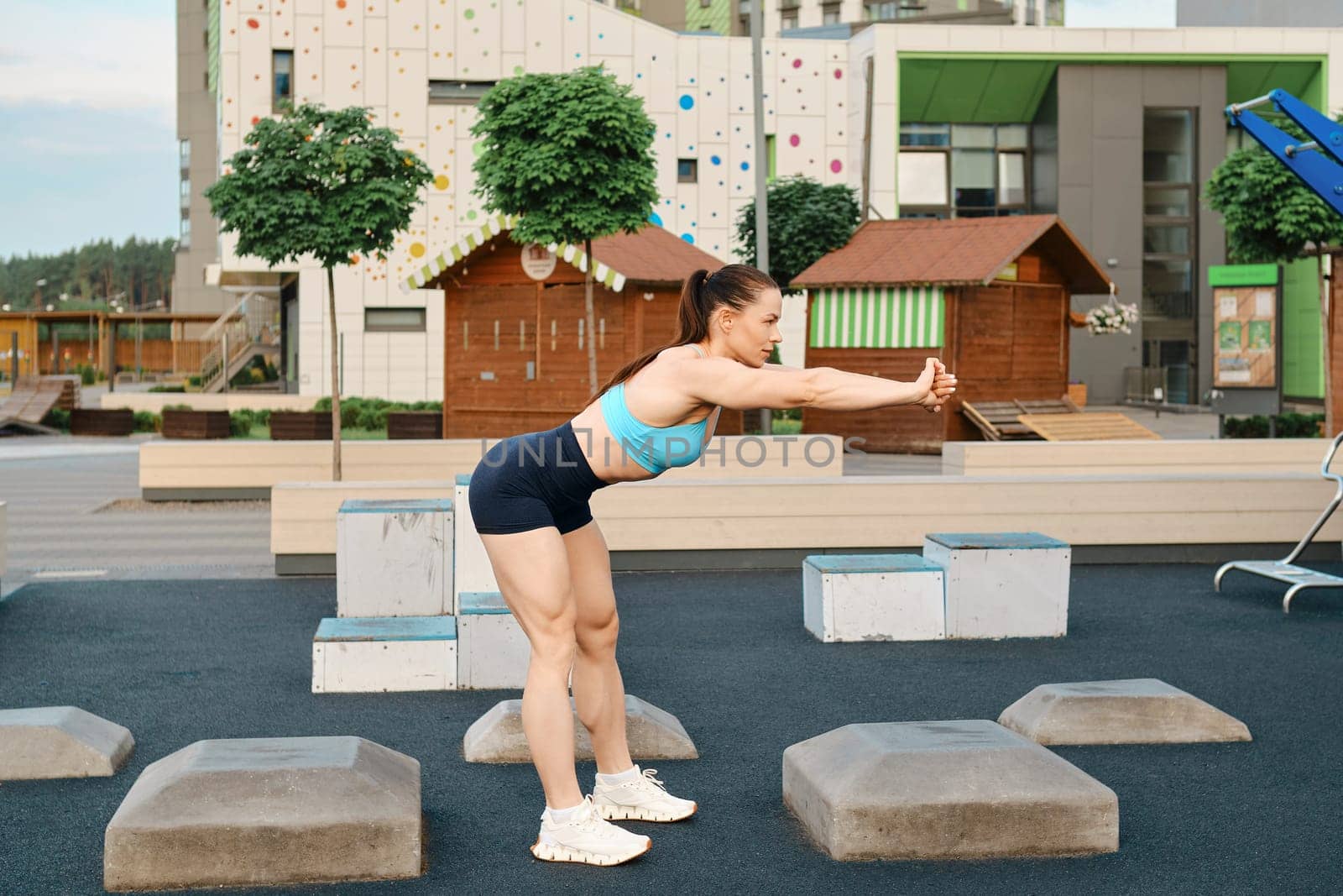 A muscular fitness woman bends forward in the sports area of a residential area in the morning