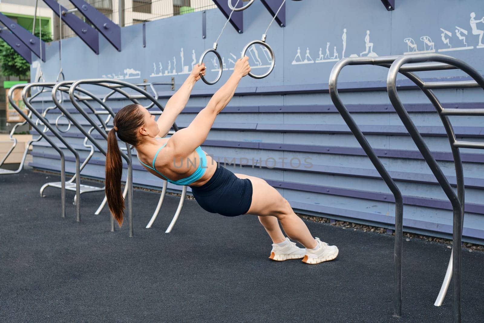 Woman doing pull-ups on rings spreading her arms to sides outdoors