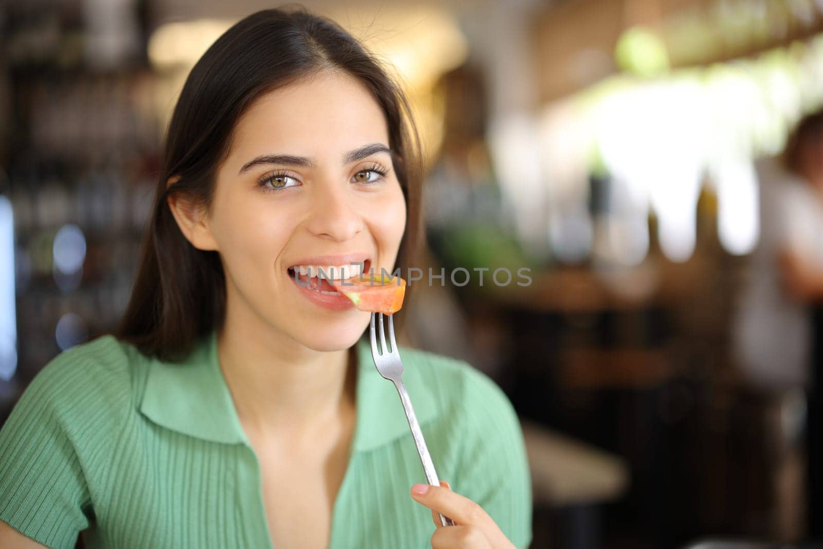 Happy restaurant customer eating tomato looking at camera