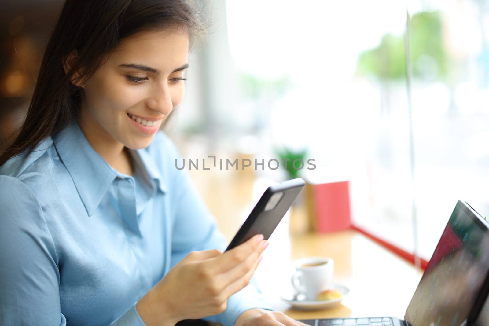 Happy woman using cell phone and tablet in a bar interior