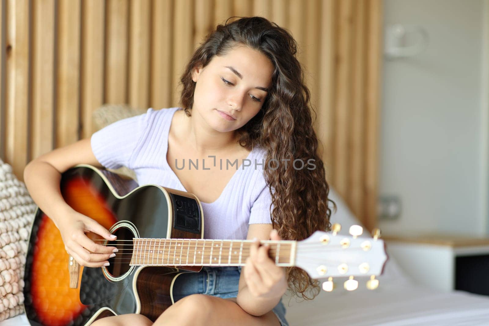 Woman playing guitar sitting on the bed in a room