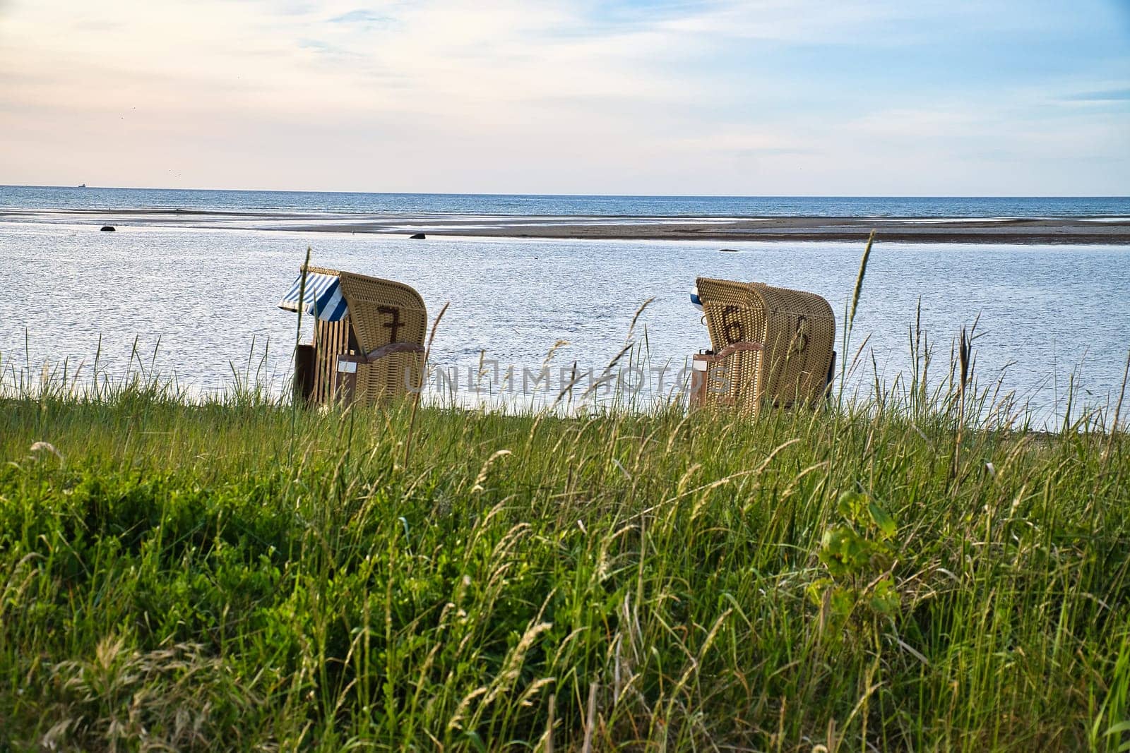 Beach chair in the sand in front of the Baltic Sea on the island of Poel at sunset. Dune grass by the sea. Landscape shot from the coast