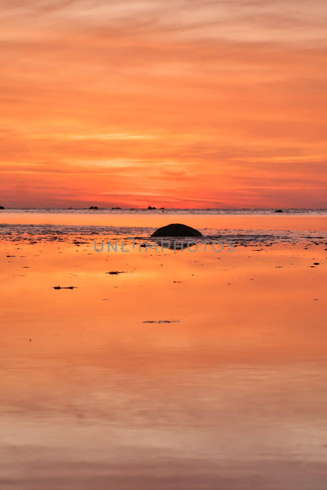 Sunset, small rock at low tide in front of the illuminated sea. Light waves. Poel island on the Baltic Sea. Nature photo from the coast