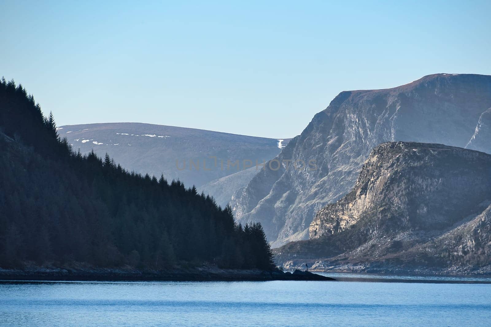 Fjord with mountains on horizon. Water glistens in the sun in Norway. Landscape photo from the north