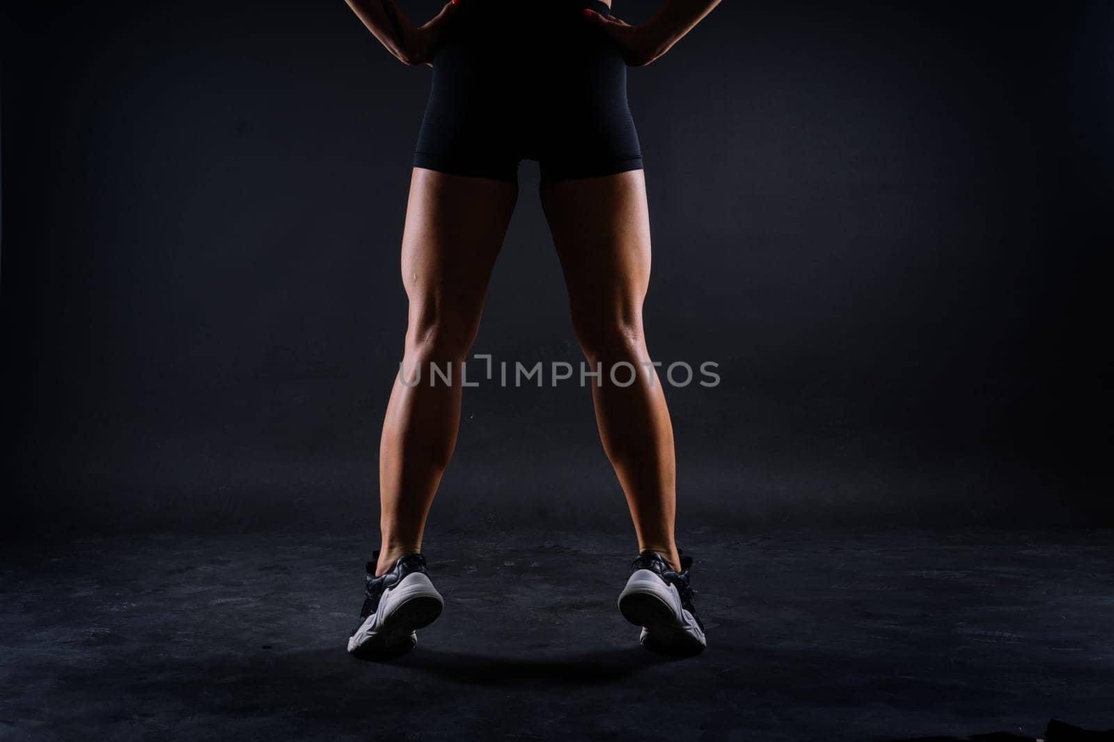 Cropped legs of a fit young woman with strong muscles over dark background