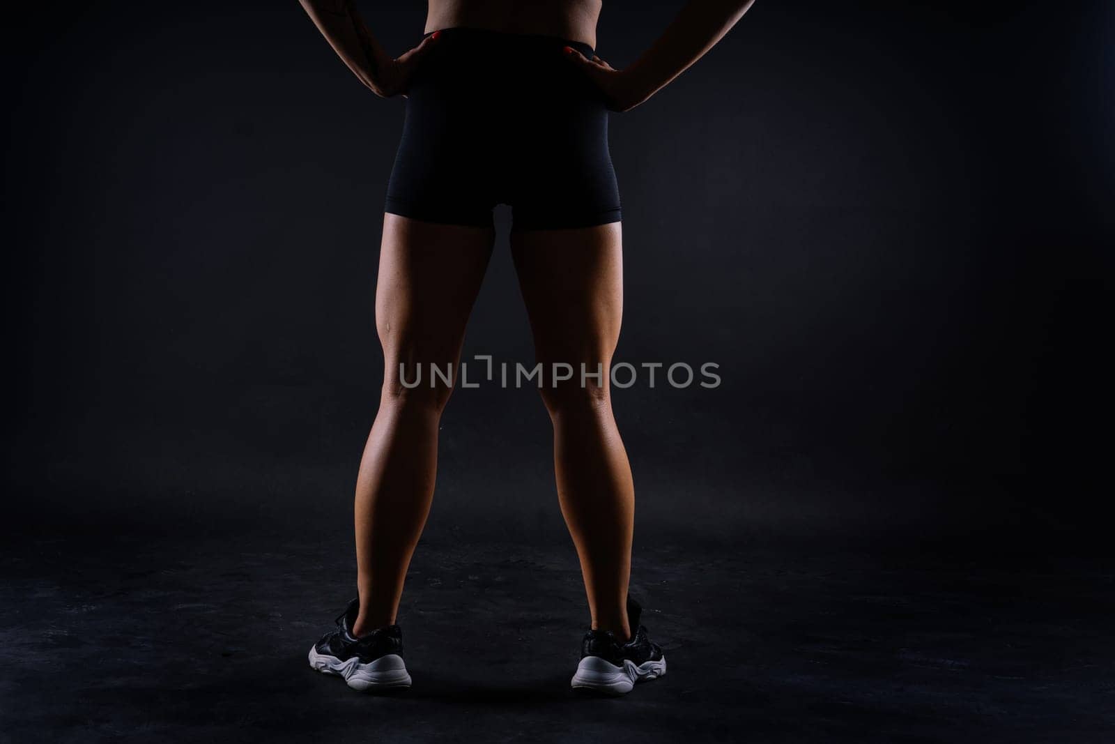 Shaped female legs in sneakers sculpted muscles, dark background
