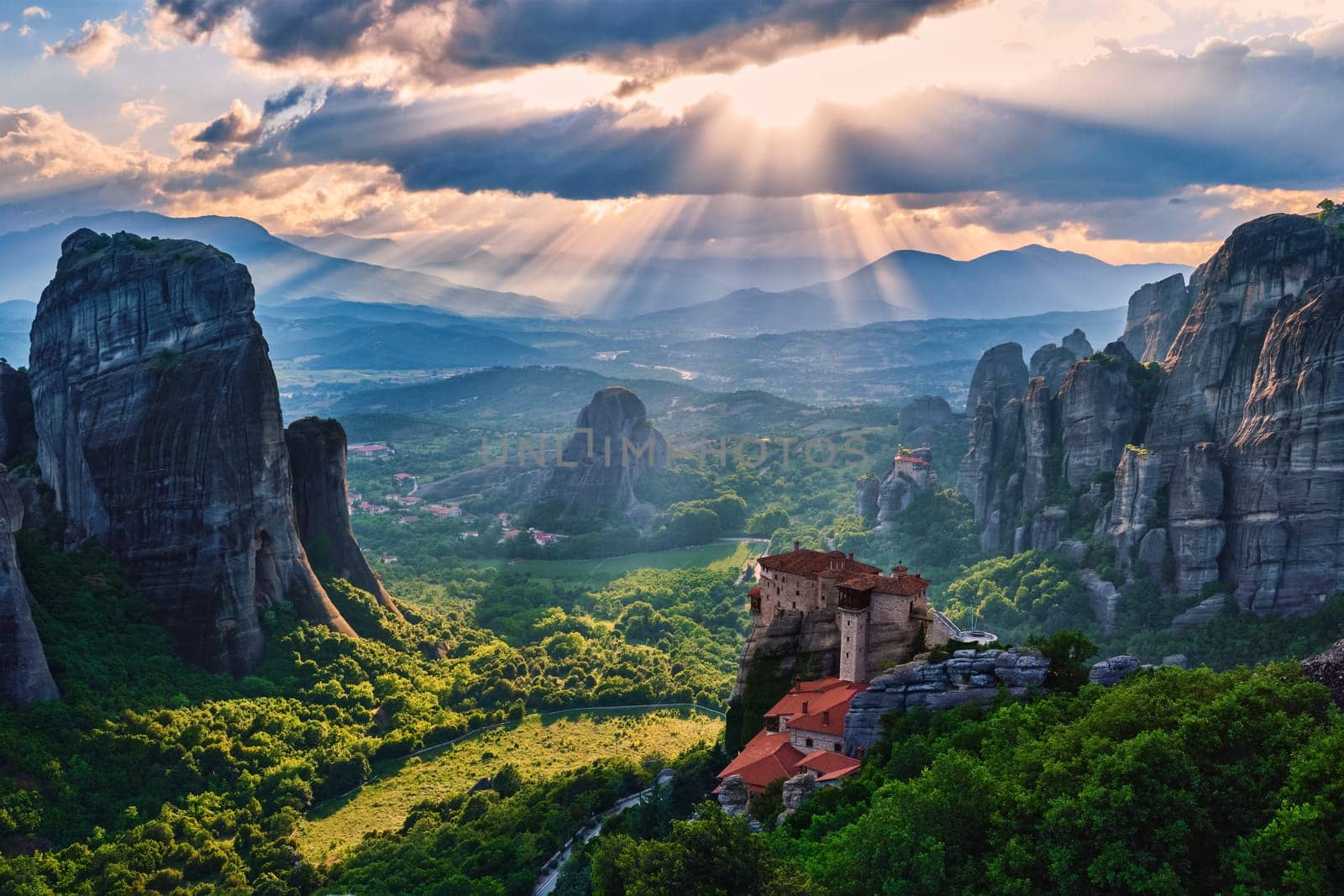 Sunset view over nunnery of Moni Agias Varvaras Roussanou and beautiful massive rocky pillars of Meteora, Greece and valley. Cloudy sky and impressive sun rays fall upon monastery. UNESCO World Heritage.