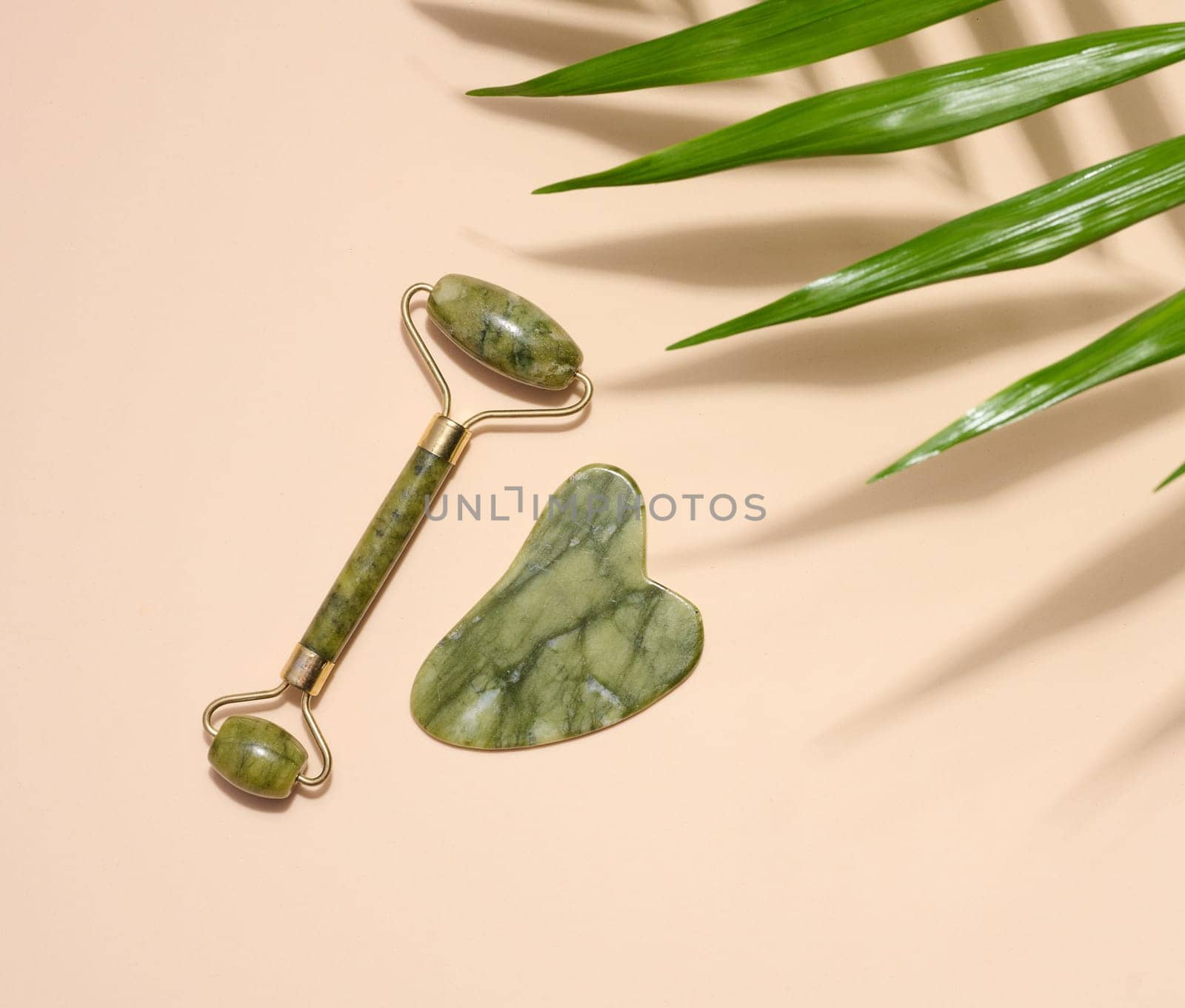 Green jade gouache massager and massage jade roller on a beige background, top view