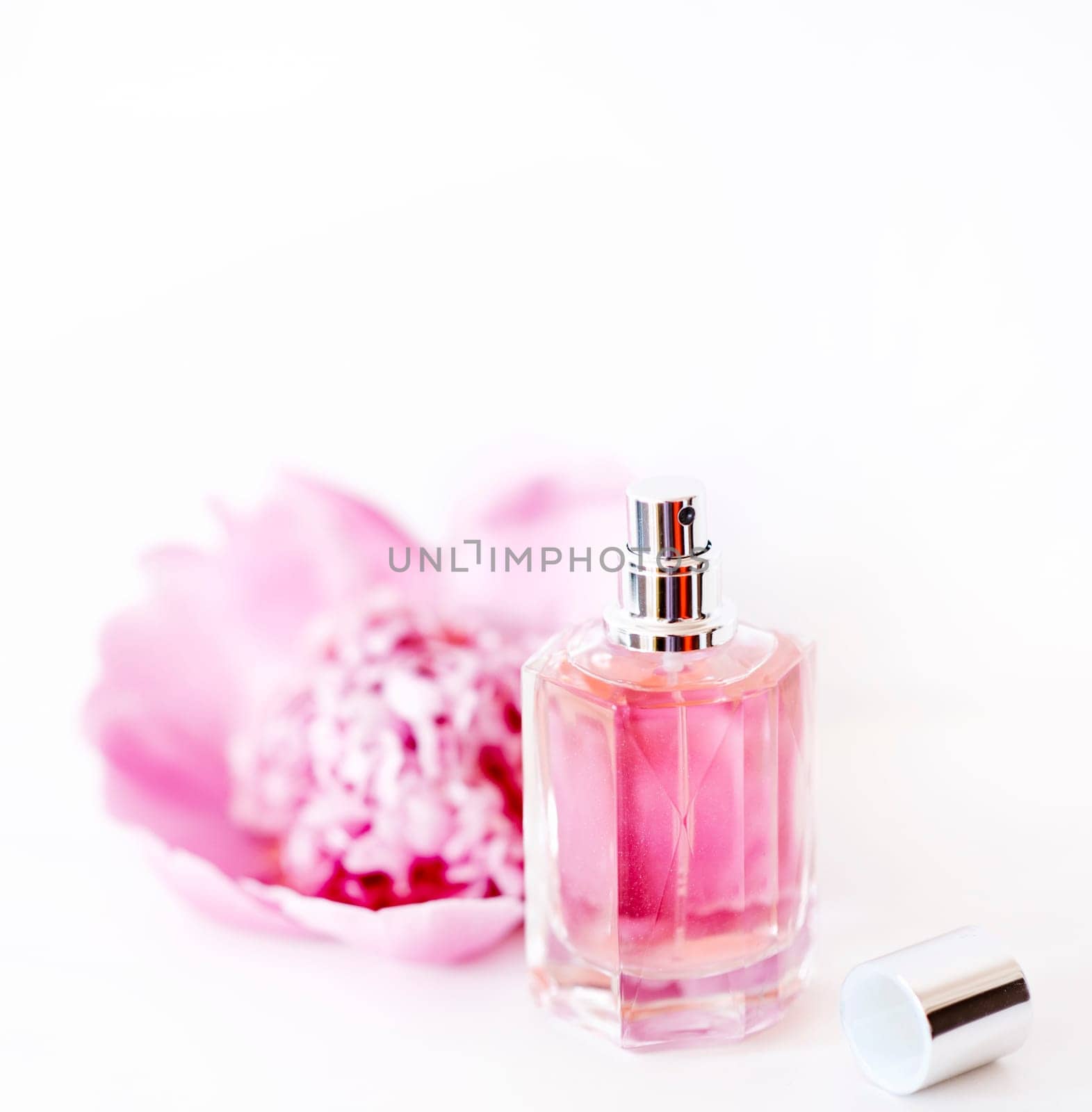Luxury perfume bottle and pink peony flower isolated on white background. Female cosmetic and girly  makeup accessory still life. Feminine cologne spray.