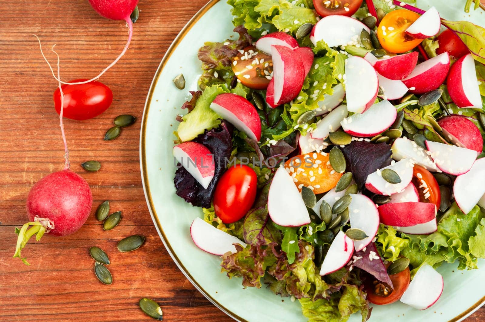 Portion of vegetable salad with radish, greens, tomato and sesame on a gray background.