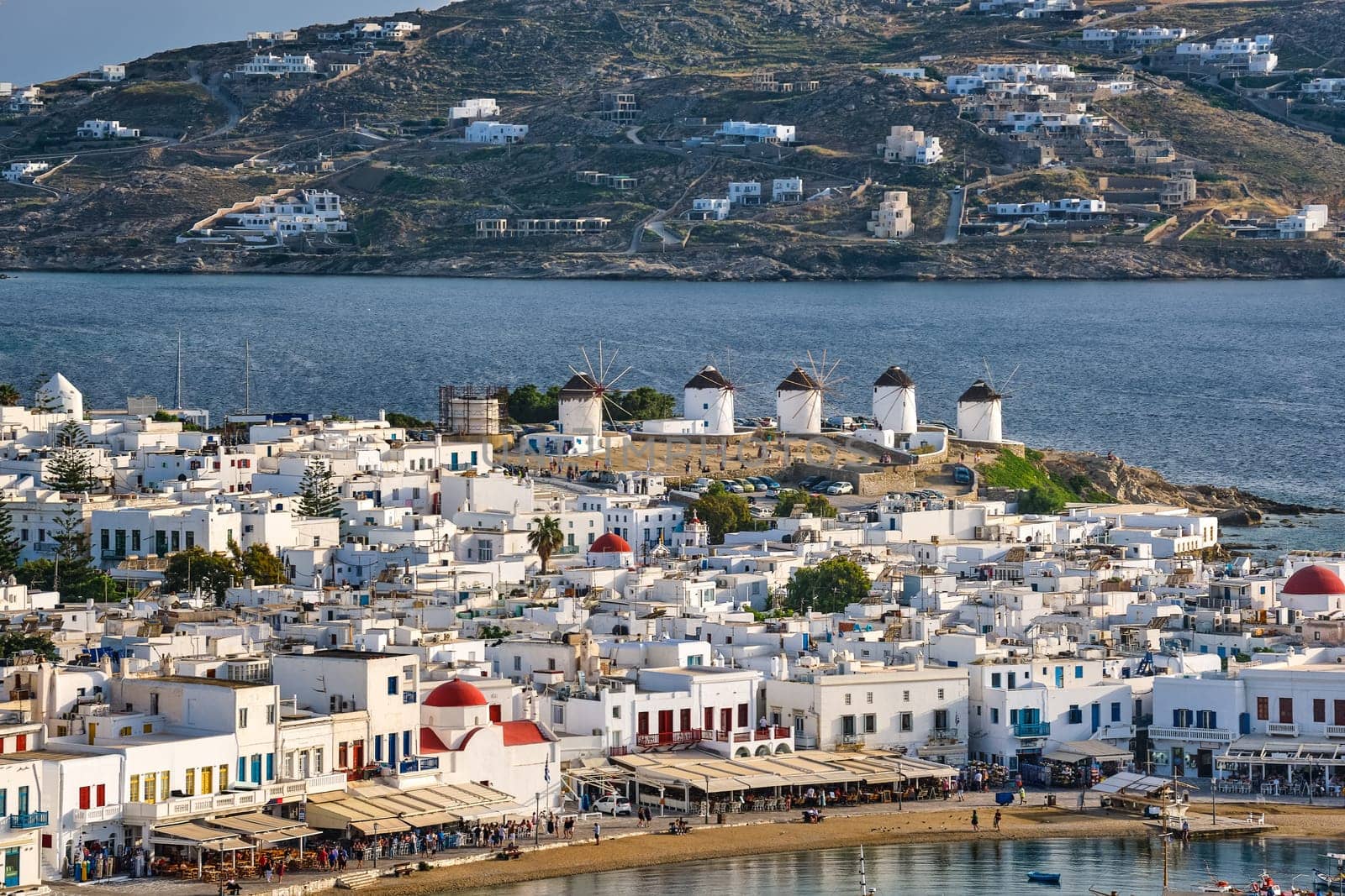 Beautiful close view, Chora, main town of Mykonos, Cyclades, Greece, and its famous landmark: white windmills Whitewashed houses with colorful windows and roofs and distant islands in background. Vacations, leisure, Mediterranean lifestyle