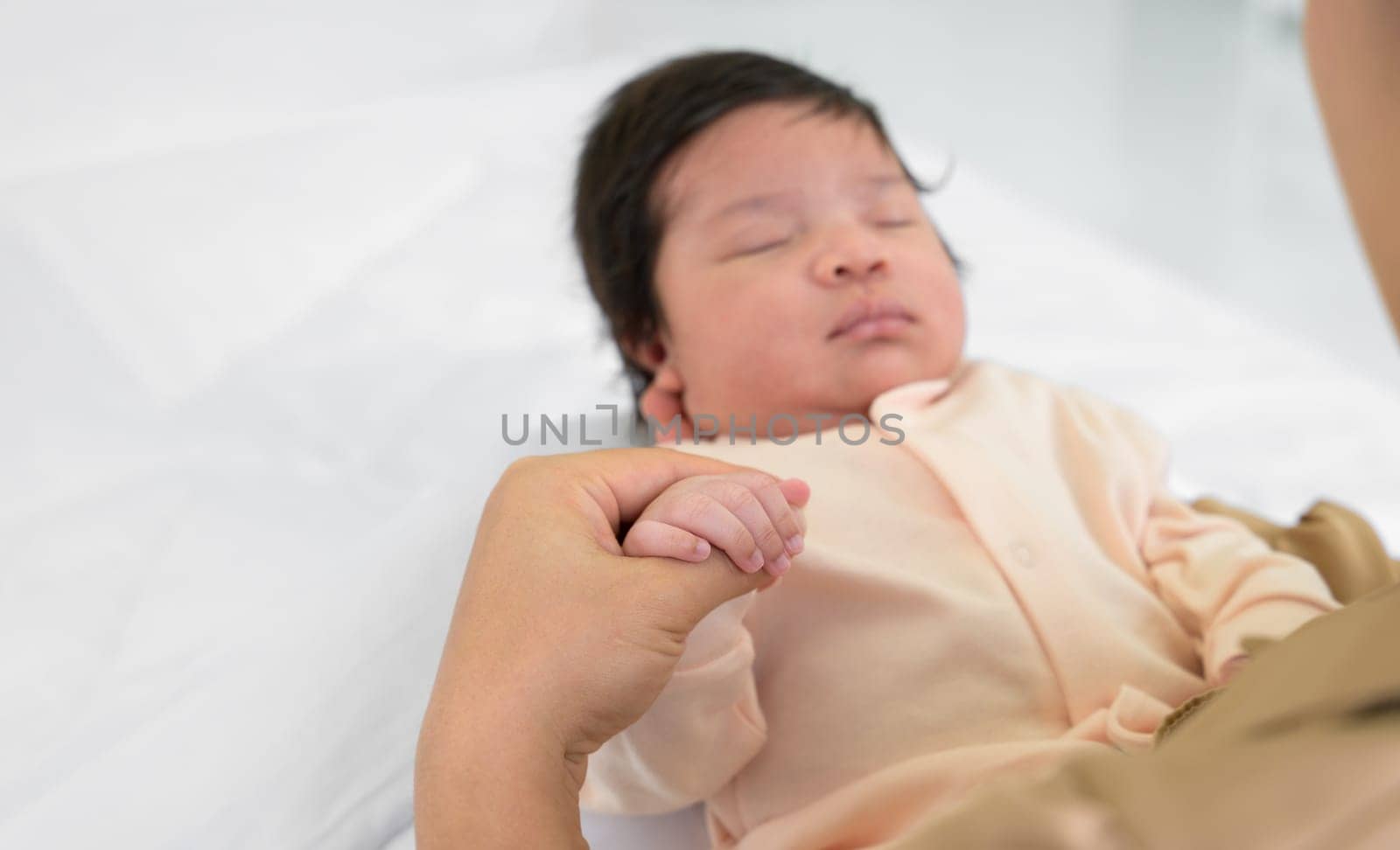 Hand of mother holding finger of newborn hand. Adorable infant girl 1 month sleeping on mom arm at home. Care, love and mothers day concept.