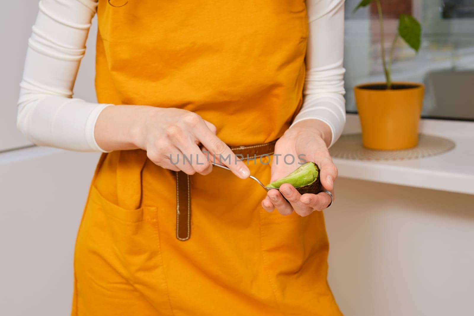 Unrecognizable woman uses spoon to scoop the avocado out of the shell