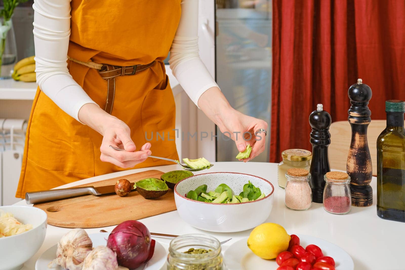 Unrecognizable woman adds slices of avocado in the bowl with probiotic salad