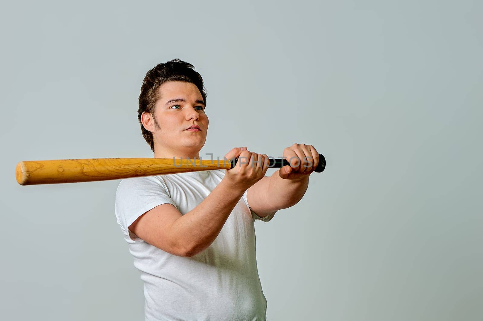 A man with a bat in his hands swings on a gray background. High quality photo