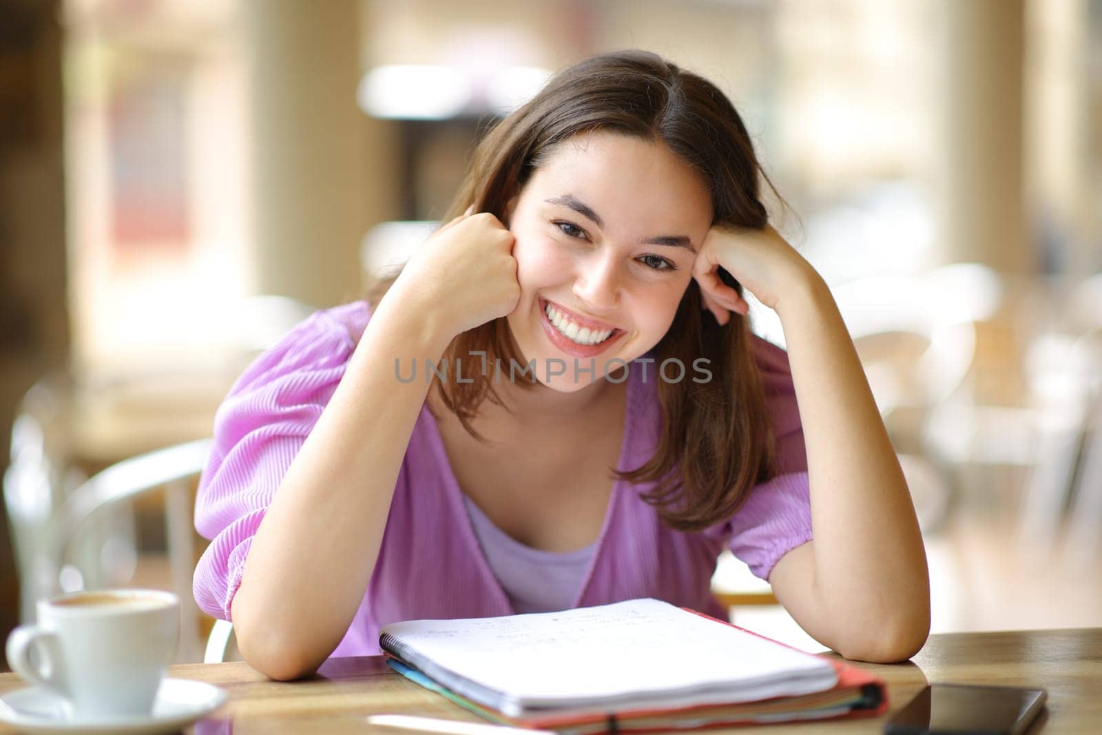 Happy student sitting in a bar terrace looks at camera