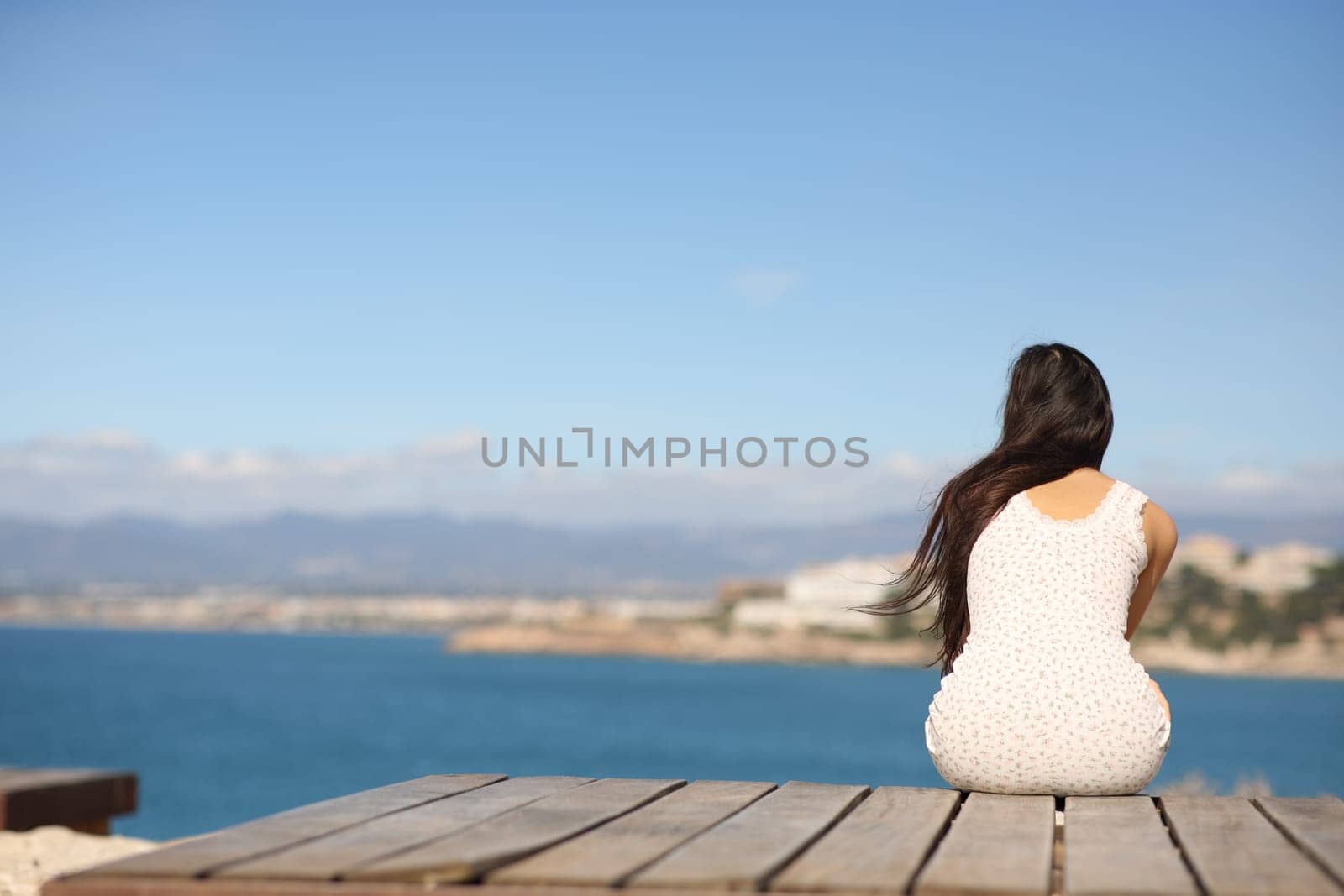 Back view portrait of a woman sitting contemplating ocean in the coast