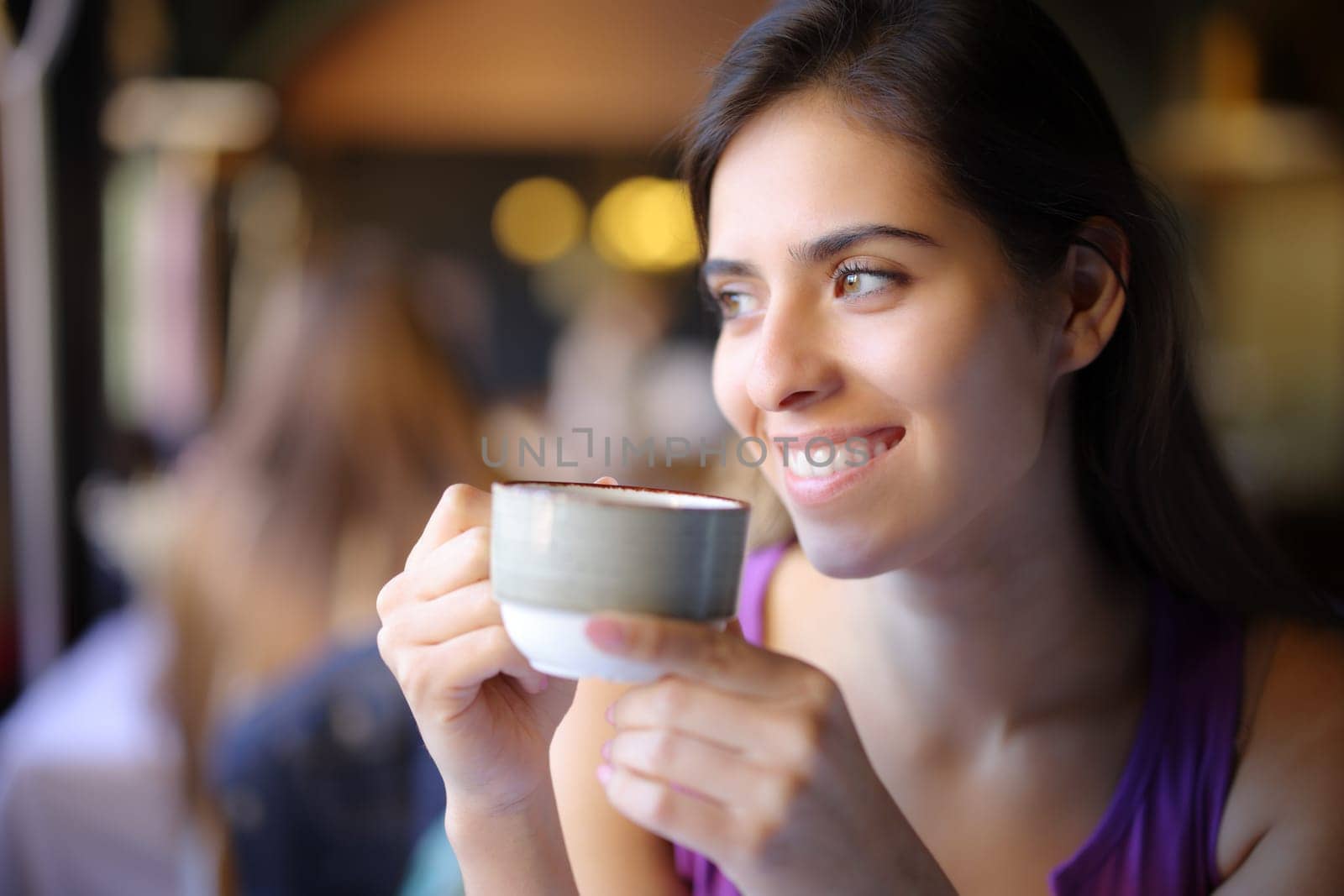 Happy woman holding coffee mug looks at side in a restaurant