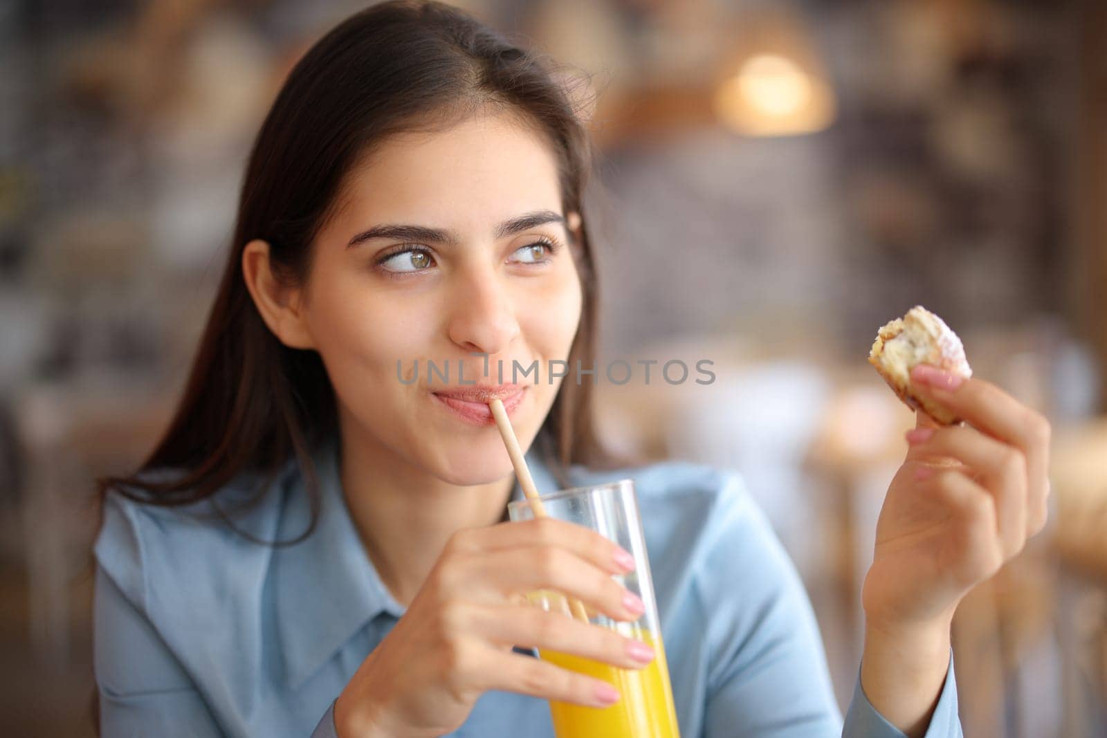 Happy woman drinking juice eating croissant in a restaurant