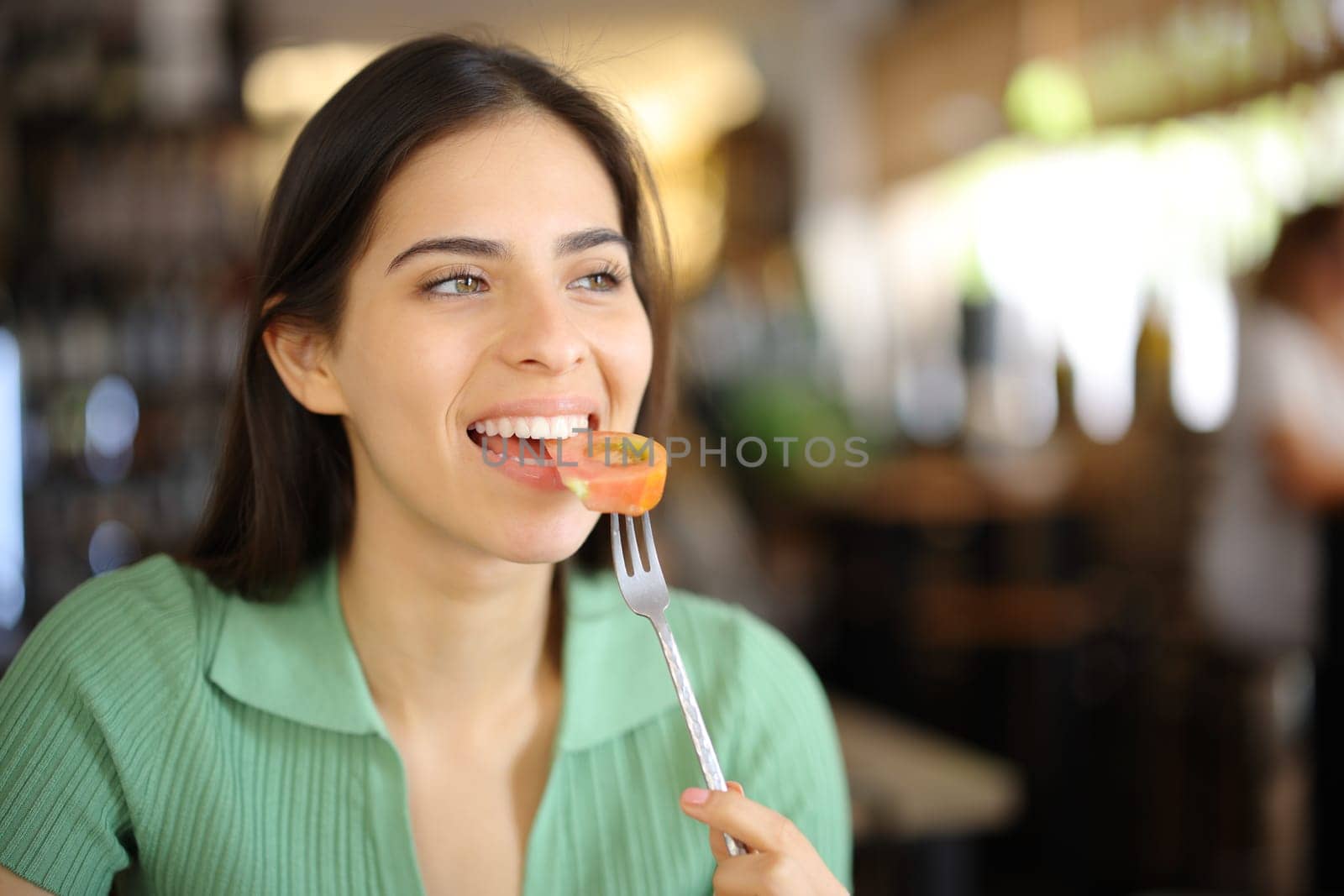Happy woman eating tomato in a restaurant interior looking away
