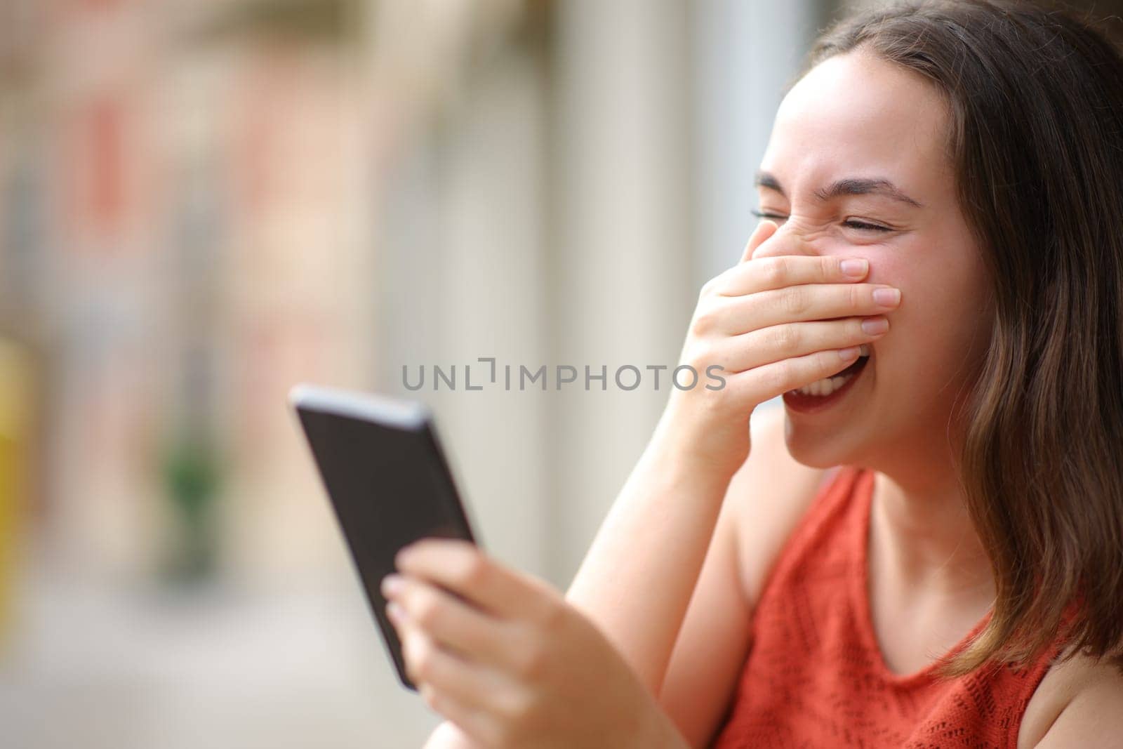 Happy woman laughing loud checking cell phone in the street