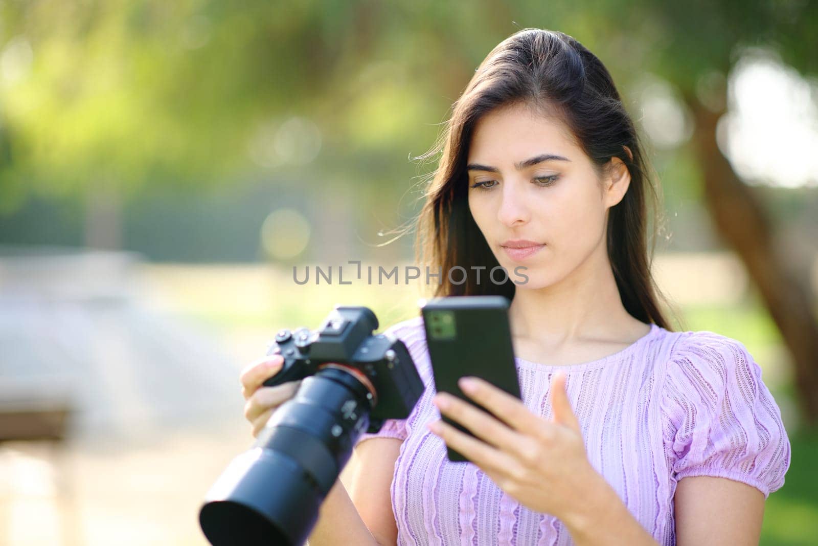 Serious photographer using mirrorless camera and smart phone in a park