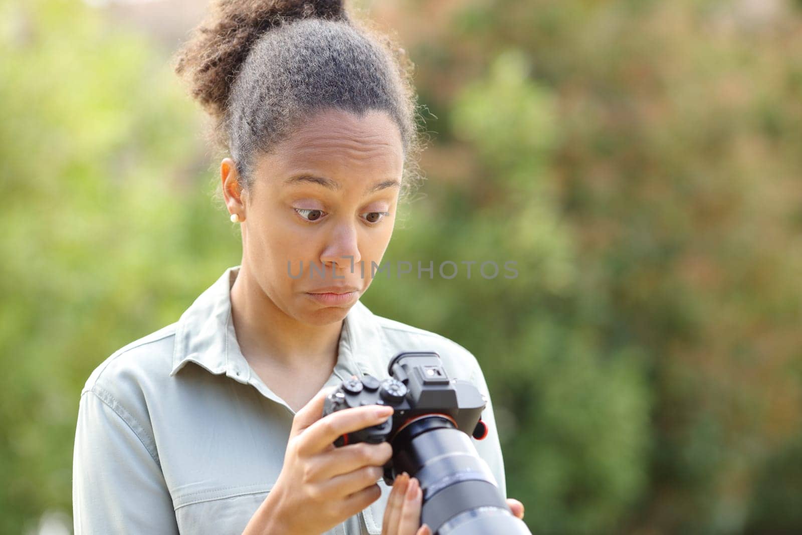 Perplexed black photographer checking mirrorless camera in a park