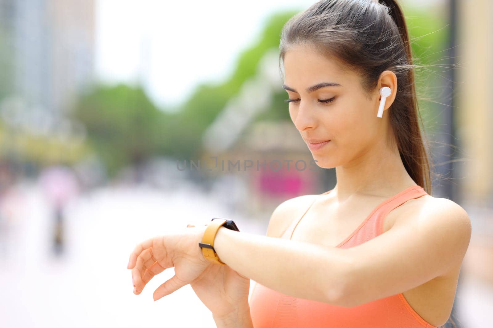 Runner with earbud checking smartwatch in the street