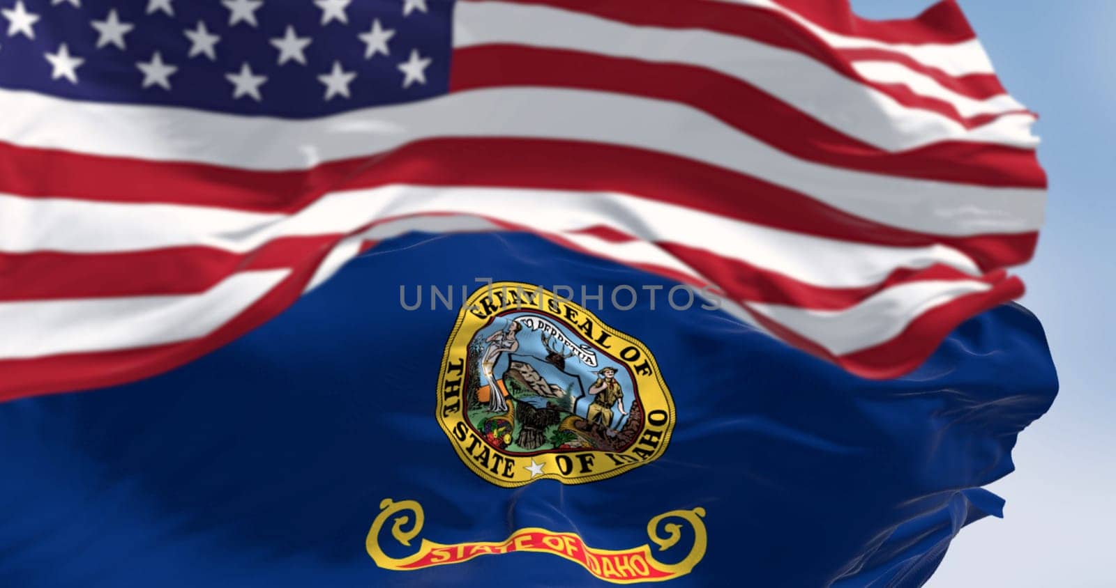 Idaho state flag waving with the national flag of the United States blurred in the foreground. 3d illustration render. Selective focus. Fluttering fabric