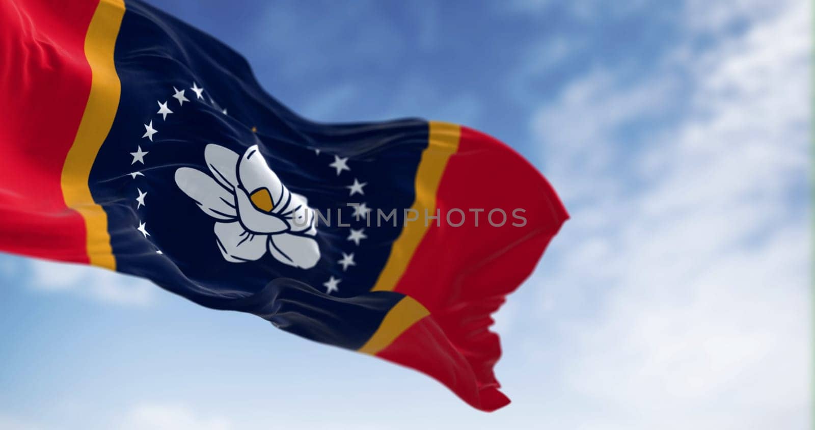 Mississippi state flag waving in the wind on a clear day. magnolia blossom, 21 stars, and the words In God We Trust. 3d illustration render. Selective focus. Fluttering fabric