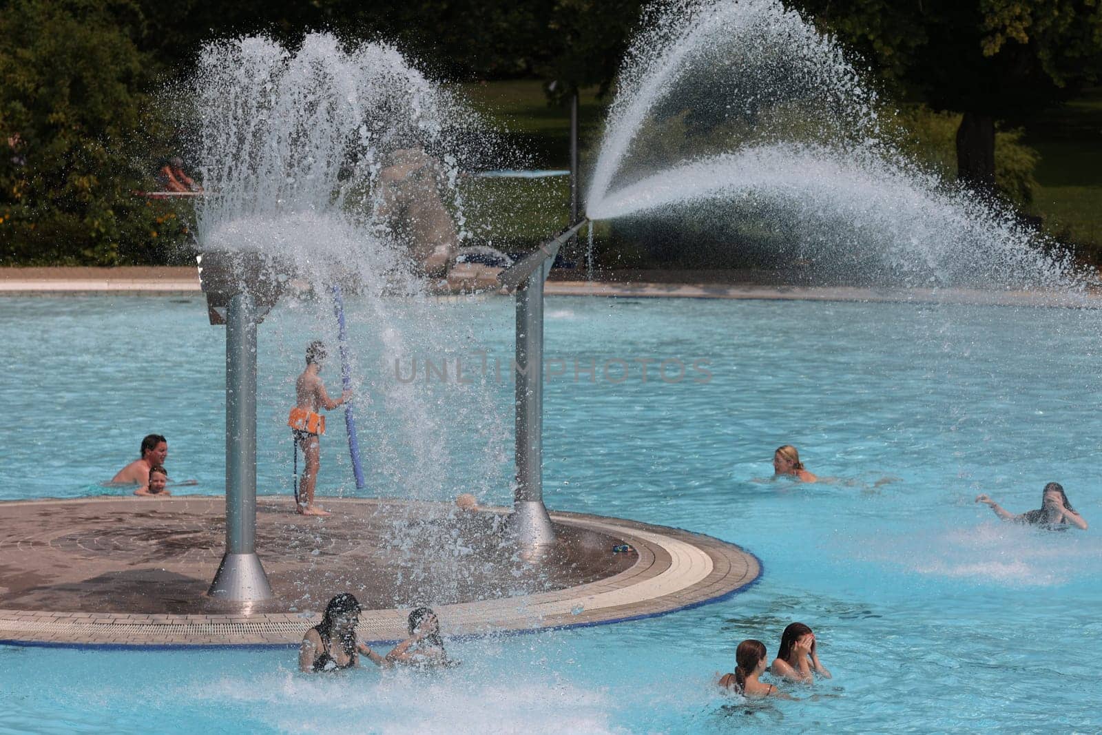 Theme picture summer -   The dog days are here - people crave to cool off at temperatures above 30 degrees Celsius,like here in the lido of Freiburg im Breisgau. Under the water fountain,young and old have fun