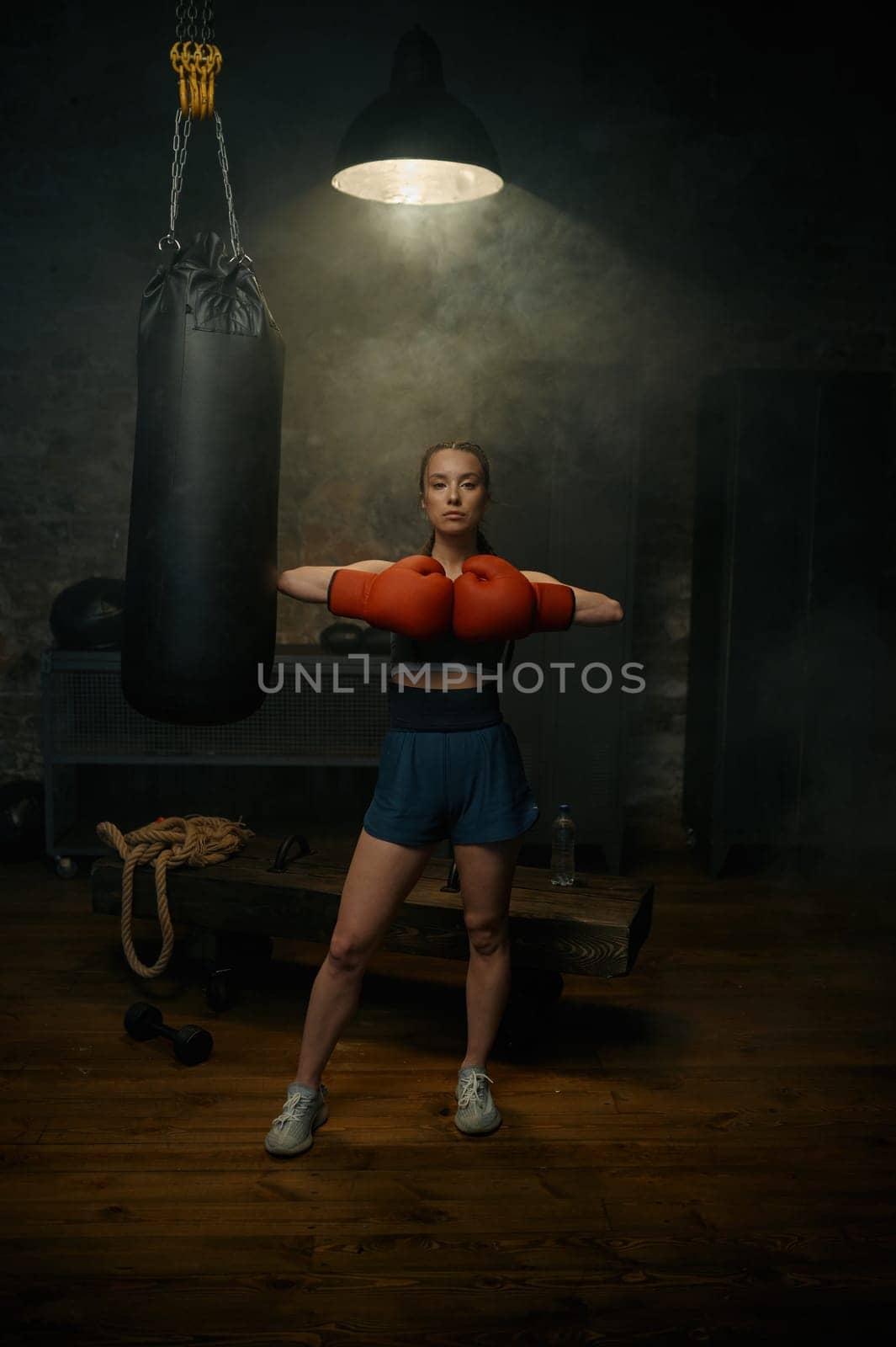 Portrait of professional beautiful sportive woman in red boxing gloves posing in gym studio