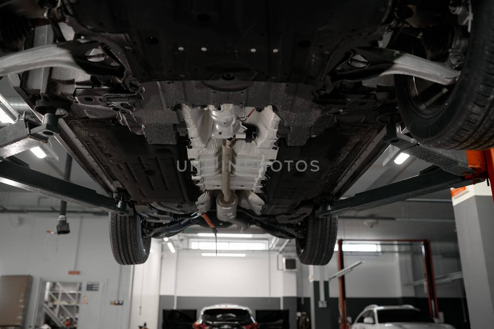 Bottom view of raised car on lift in repair garage. Visible details and structure of suspension or elements of exhaust system