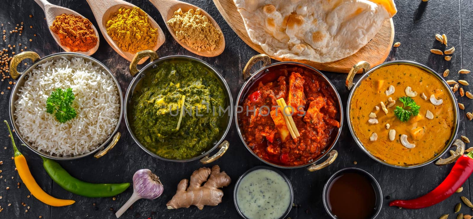 Composition with indian dishes: madras paneer, palak paneer and shahi paneer with basmati rice served in original indian karahi pots.