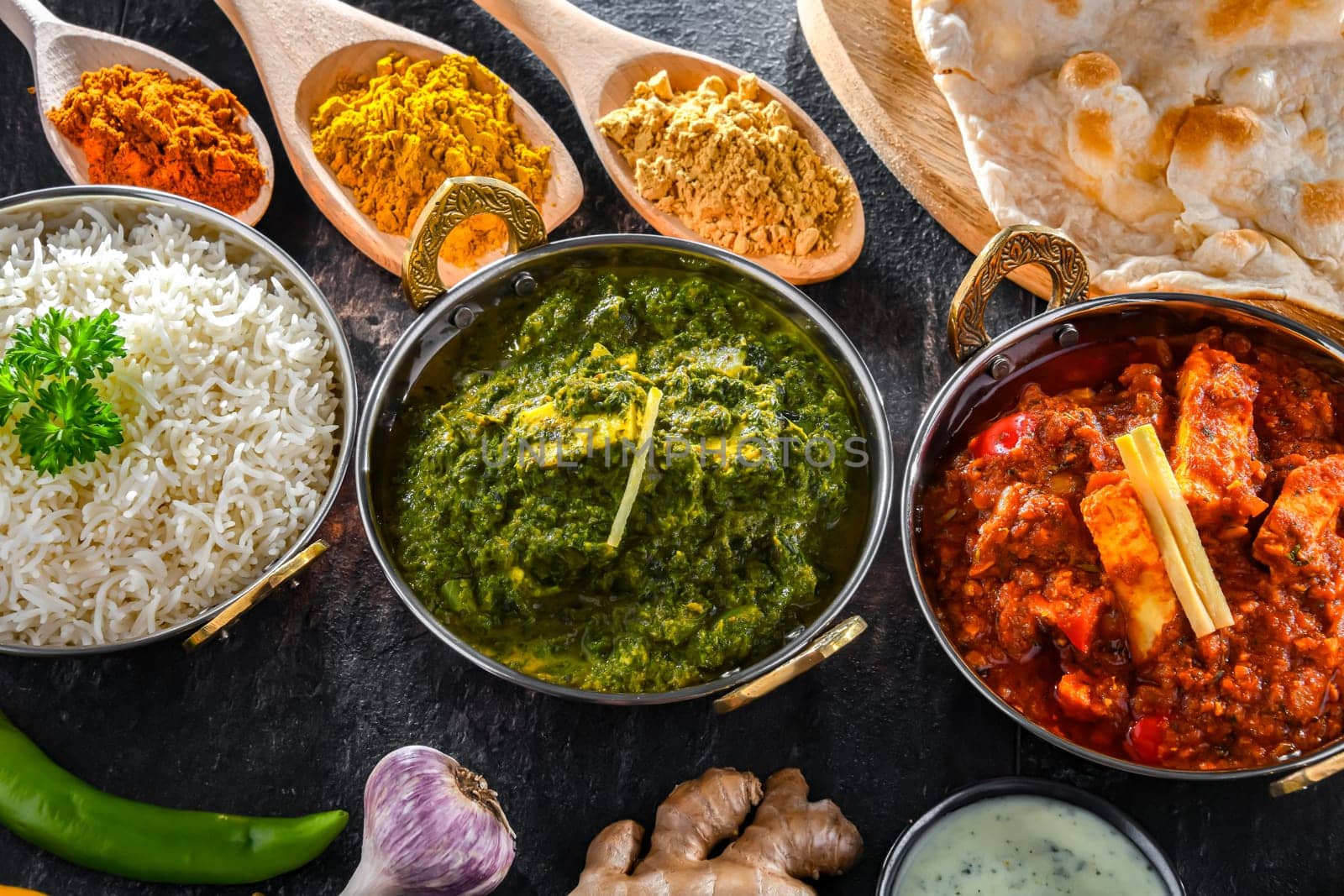 Composition with indian dishes: madras paneer, palak paneer and shahi paneer with basmati rice served in original indian karahi pots.