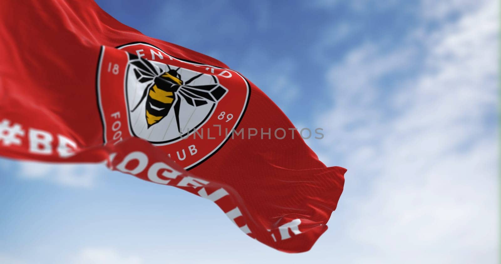 London, UK, Feb 19 2023: Brentford Football Club flag waving in the wind on a clear day. Circular emblem with a bee inside on red. Illustrative editorial 3d illustration render