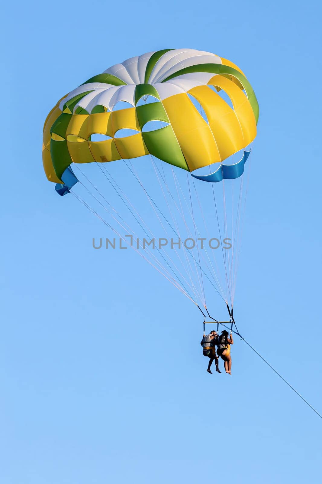 FIUMEFREDDO DI SICILIA, SICILY, ITALY - AUGUST 12, 2022 A black couple in bathing suits and life jackets pulled and flying with a yellow parachute near the shore