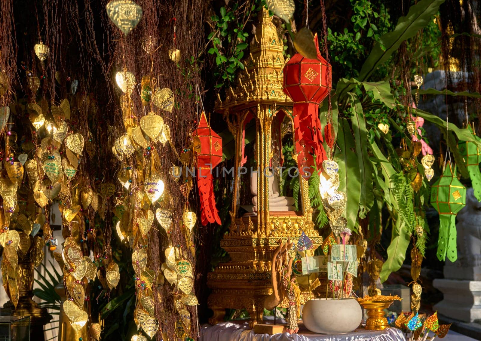 Traditional Thai Buddha altar as busabok with money and incense sticks offerings, colorful Lanna lanterns. Bodhi tree with golden leaves with wishes and promises in many languages. Selective focus, blurred background. Golden Mount, Bangkok, Thailand