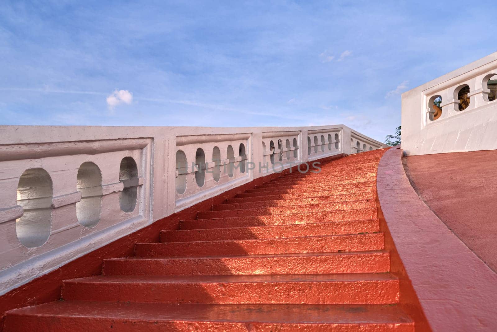 Red sunlit stairs and white banisters leading upwards at blue sky. Concept of ascension, opportunity, richness. Steps up to temple of Wat Saket or Golden Mount, Bangkok, Thailand.