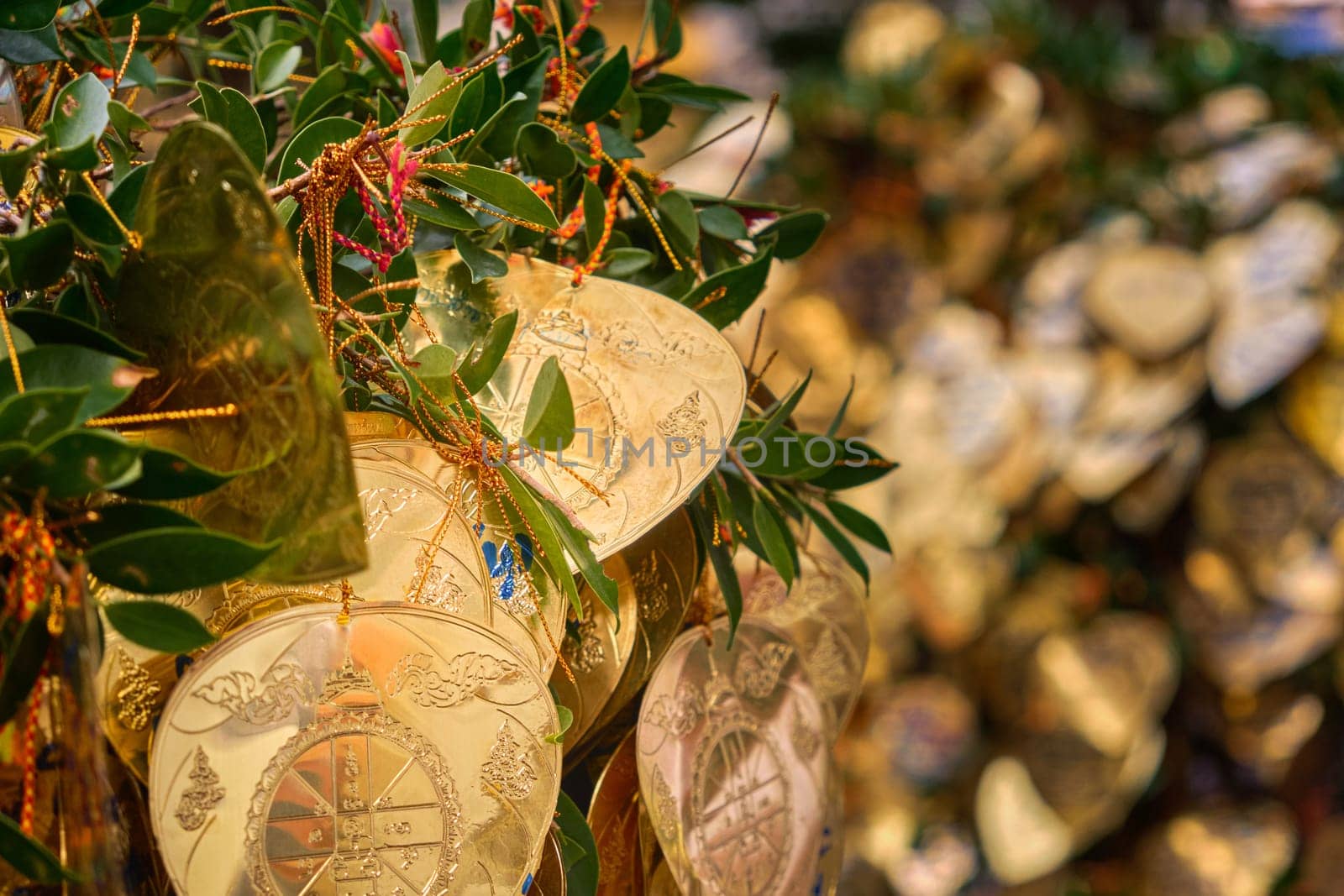 Traditional form of prayer in Thailand, artificial golden leaves with handwritten wishes in many languages tied to Bodhi tree branches. Selective focus, blurred background. Religion, rituals, worship, wishes, multi-language.