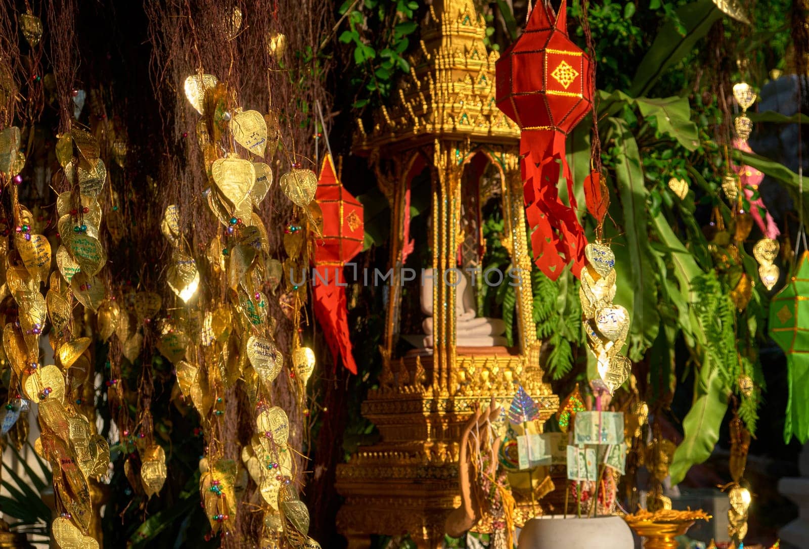 Traditional Thai Buddha altar as busabok with money and incense sticks offerings, colorful Lanna lanterns. Bodhi tree with golden leaves with wishes and promises in many languages. Selective focus, blurred background. Golden Mount, Bangkok, Thailand