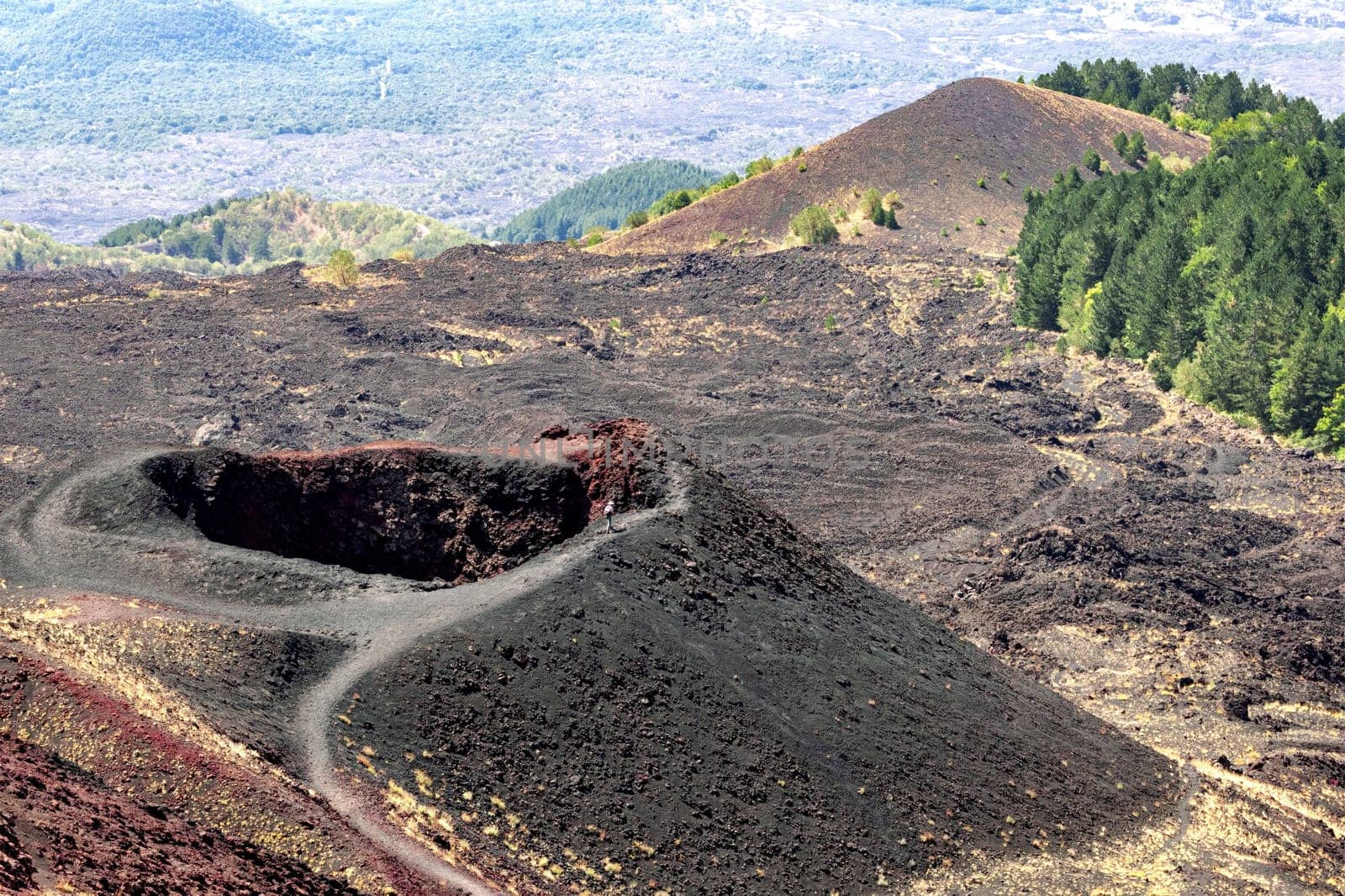 Tourist walking on the edge of a small crater on the slopes of Mount Etna on the island of Sicily, Italy