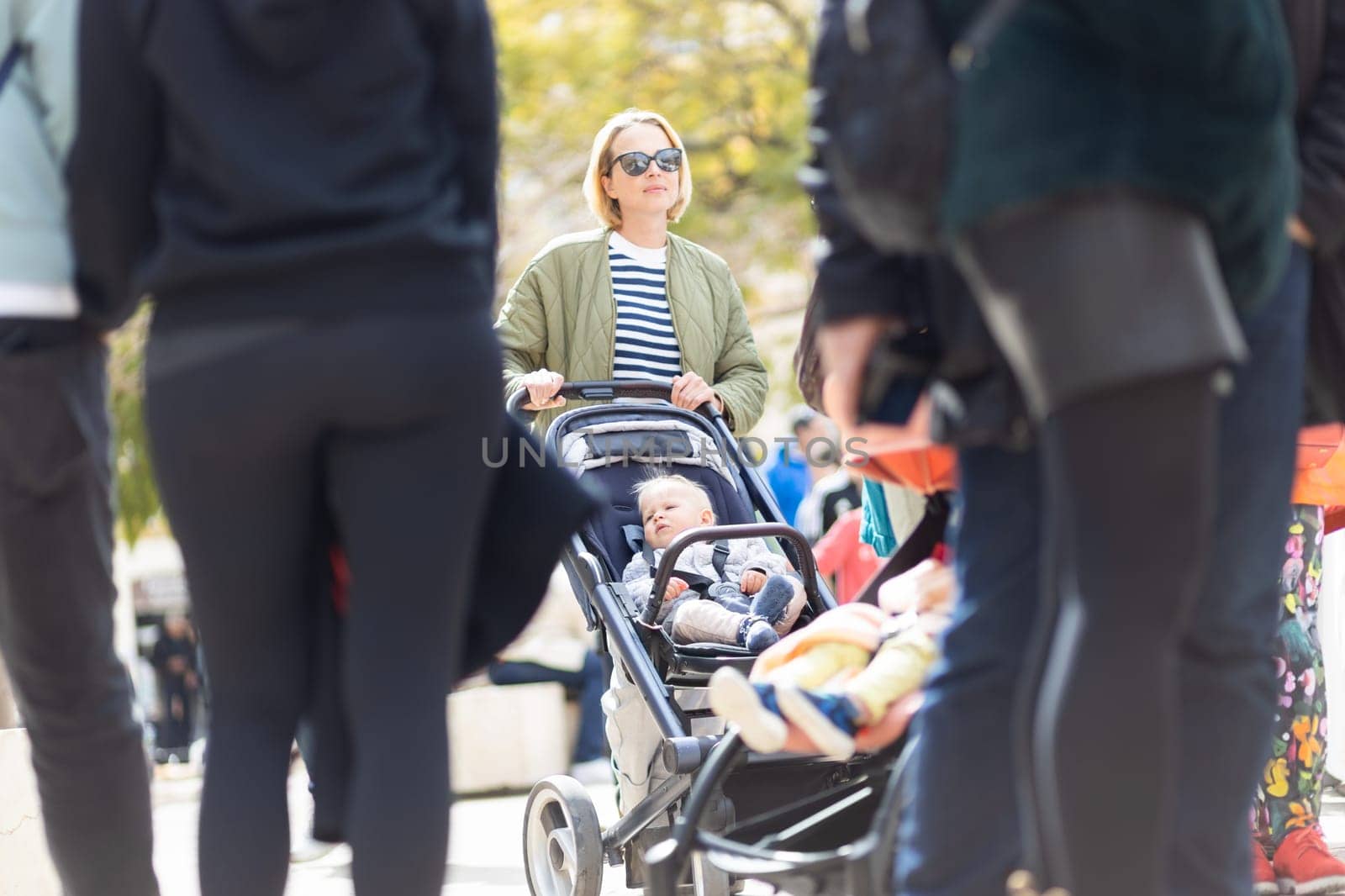 Mother walking and pushing his infant baby boy child in stroller in crowd of people wisiting sunday flea market in Malaga, Spain