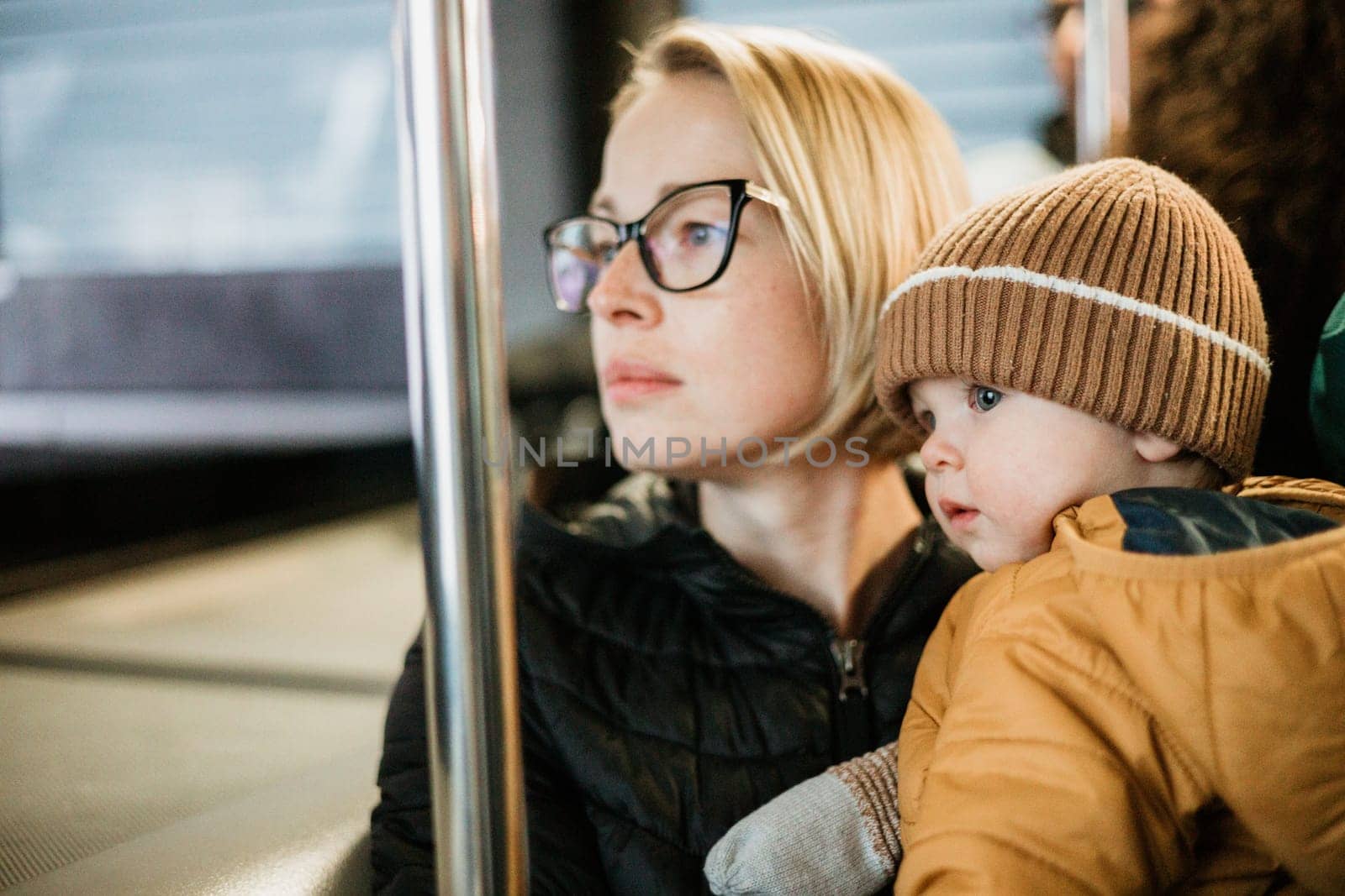 Mother carries her child while standing and holding on to the bus. Mom holding her infant baby boy in her arms while riding in a public transportation. Cute toddler boy traveling with his mother