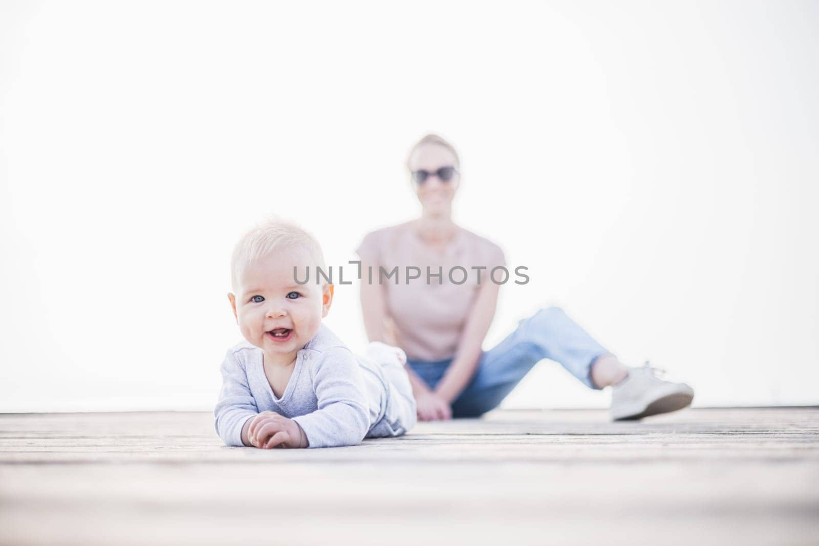 Happy family. Young mother playing with her baby boy infant oudoors on sunny autumn day. Portrait of mom and little son on wooden platform by lake. Positive human emotions, feelings, joy